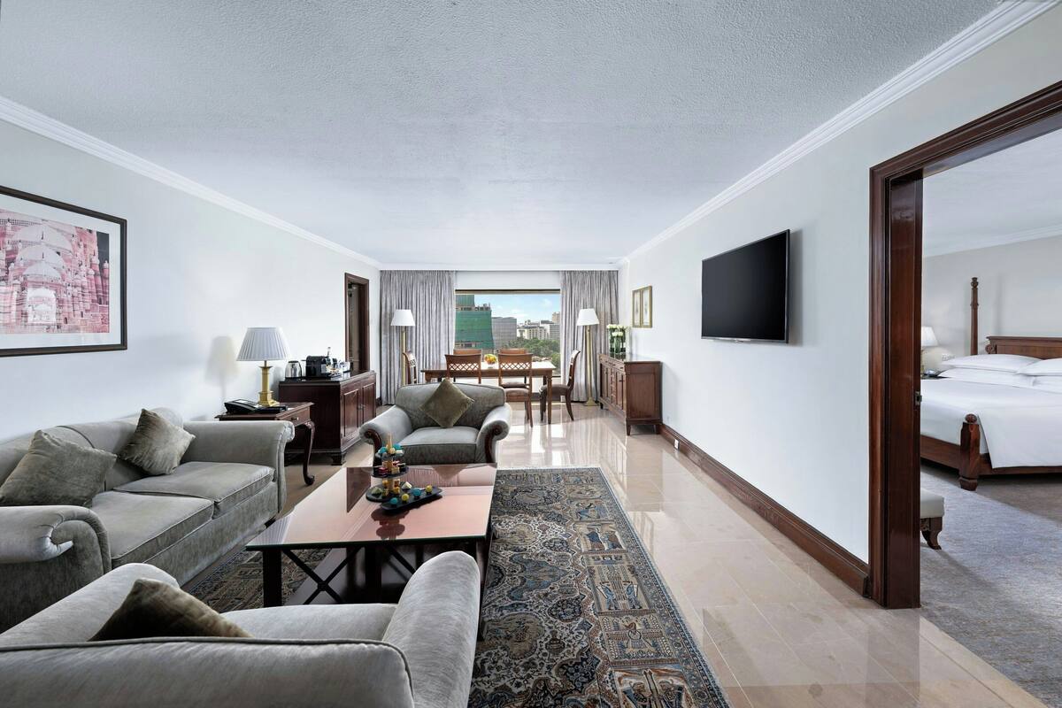 A hotel room with a sofa, armchair, coffee table, TV, and a bed.