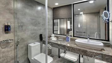 A modern bathroom with a toilet, bidet, and a large mirror with a built-in light.
