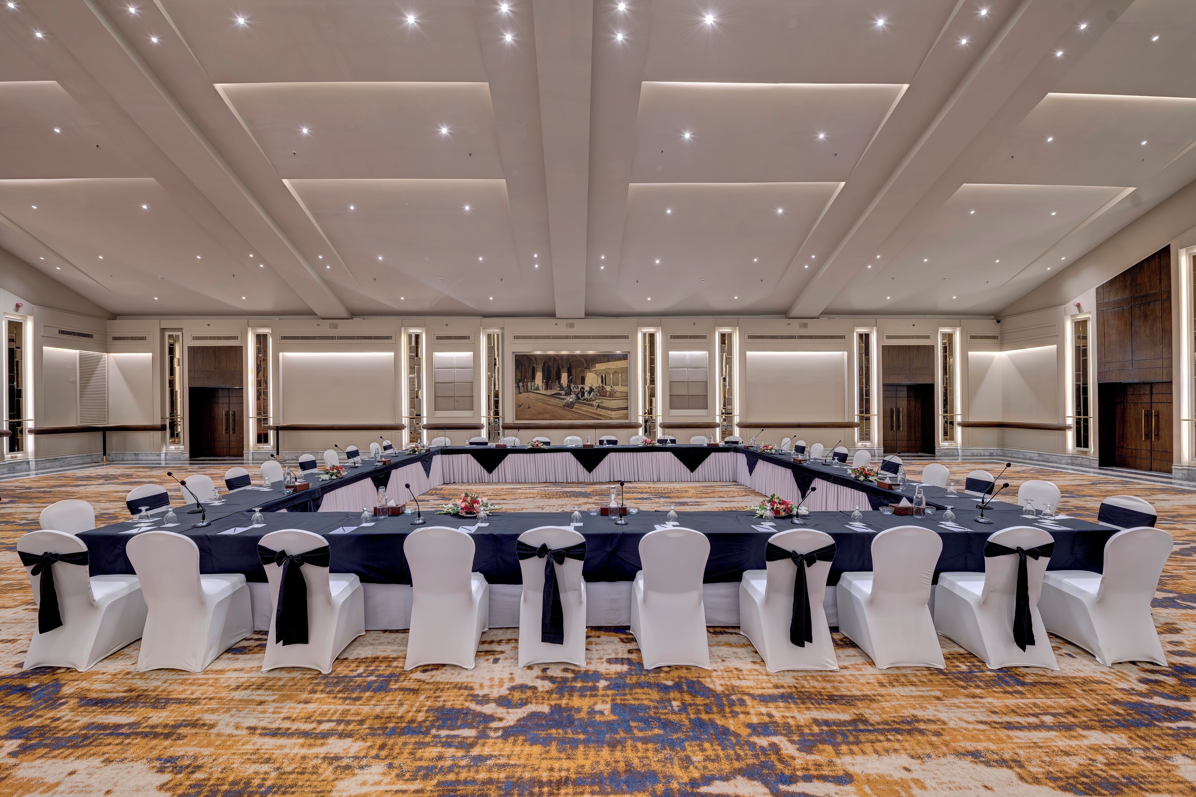 A conference room with a long table, white chairs with black sashes, and a carpeted floor.