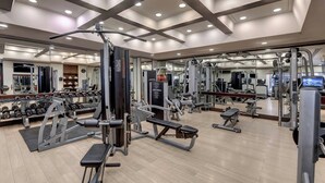 Un gimnasio con diversos equipos de ejercicio, espejos y piso de madera.