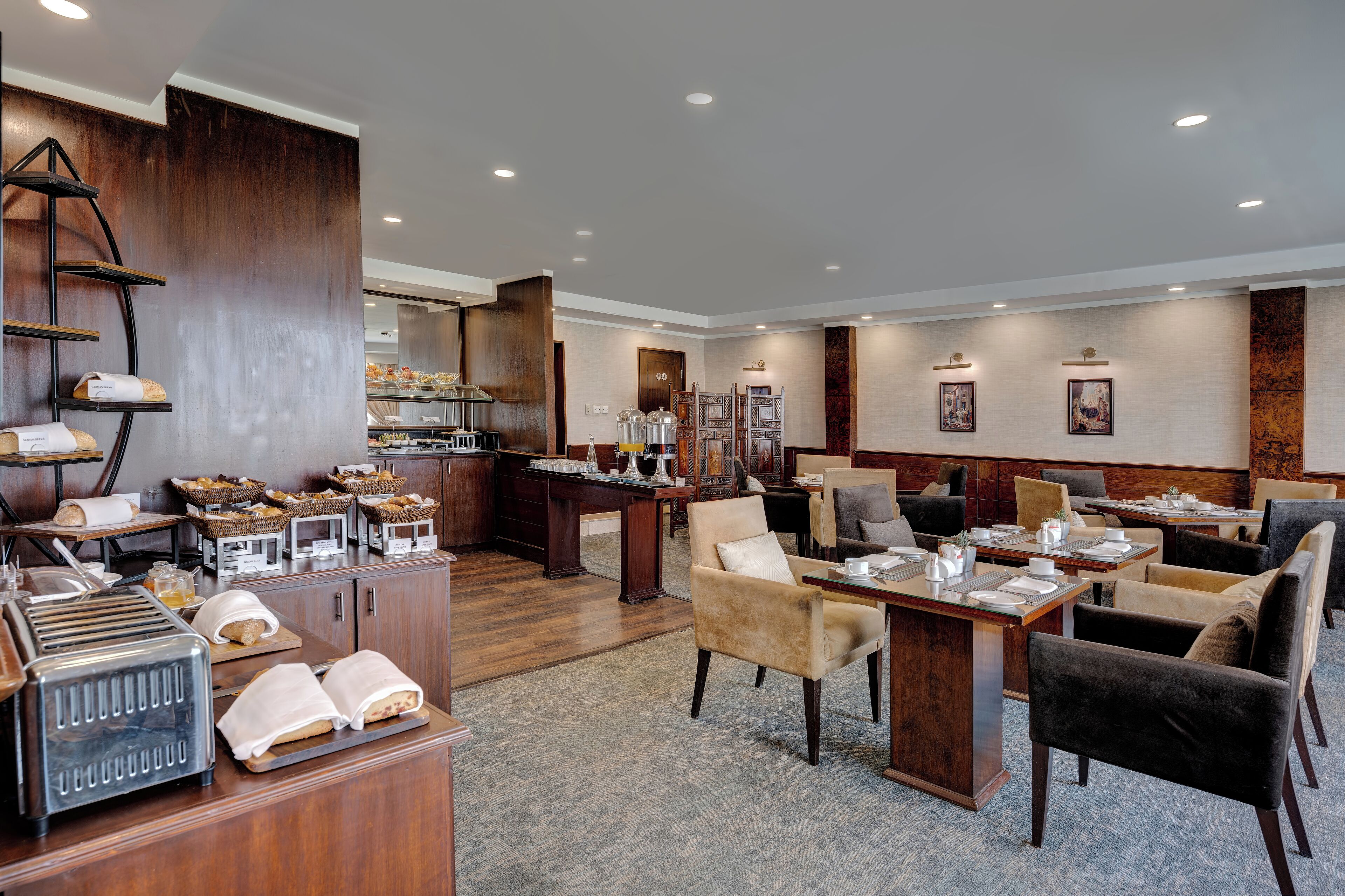 A hotel dining area with wooden furniture, a buffet setup, and a bar area.