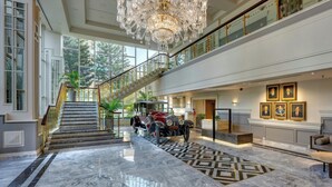 Un hall imponente con candelabro, suelo de mármol, un coche antiguo y una escalera.