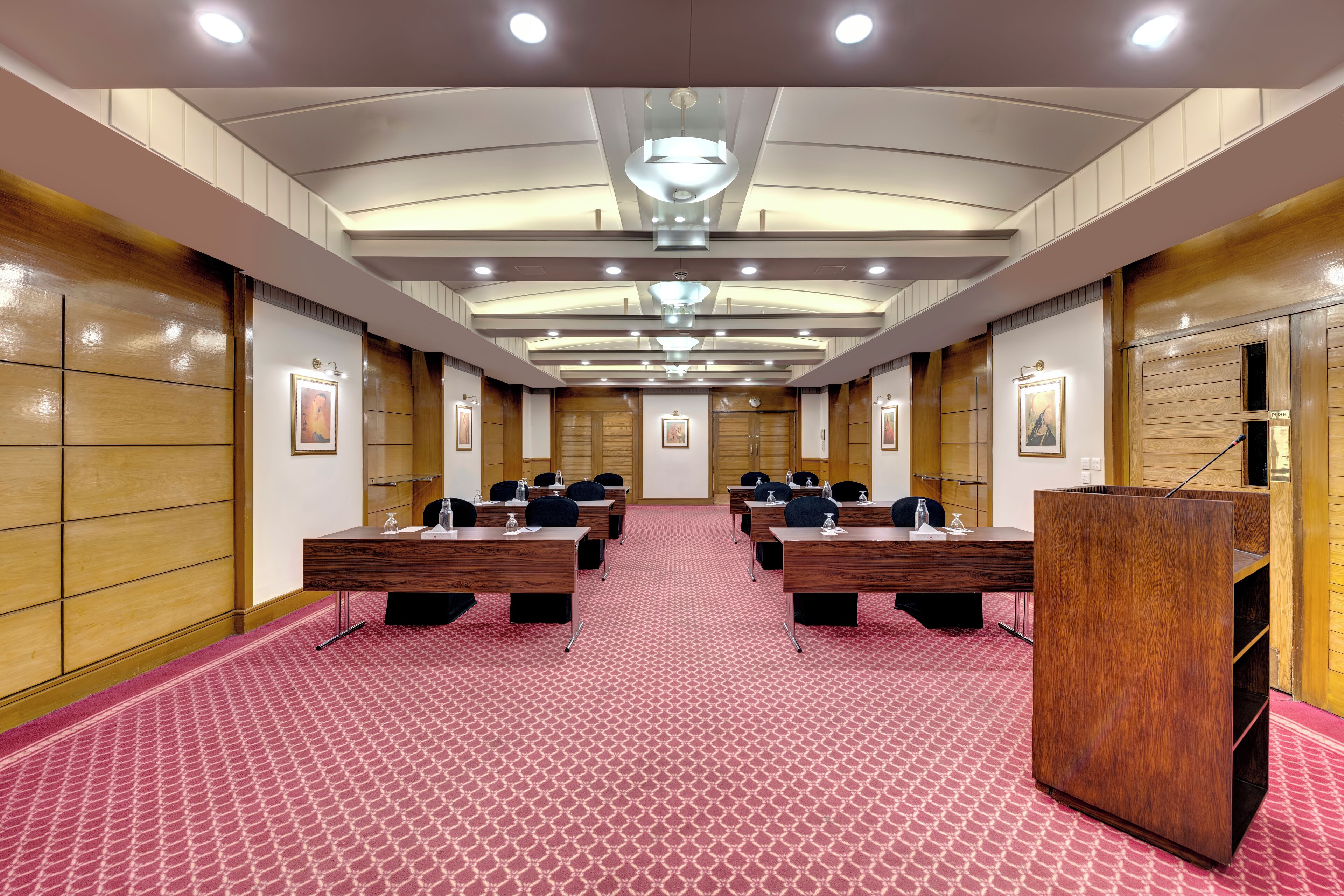 A conference room with a long table, multiple chairs, a podium, and framed pictures on the walls.