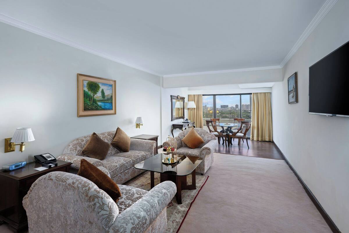 A hotel room with a sofa set, a coffee table, a TV, a painting, and a view of the city.