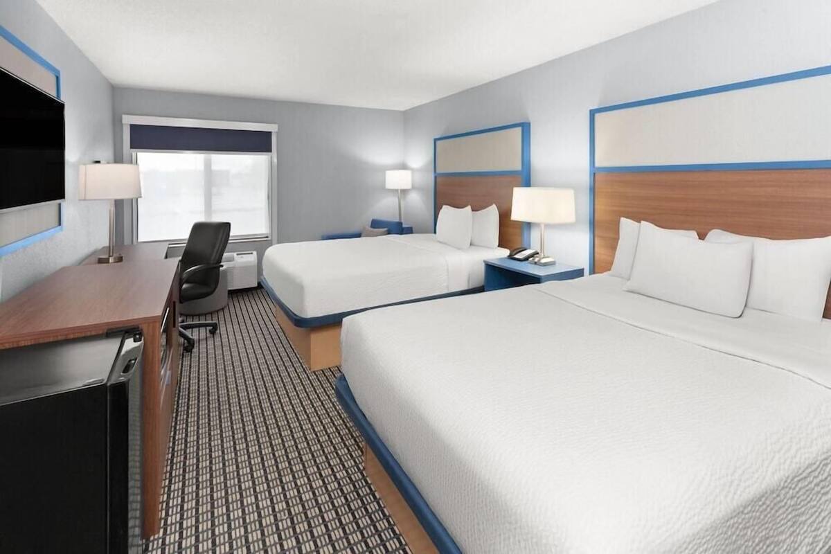 A hotel room with two beds, a desk, a chair, a TV, and a window.
