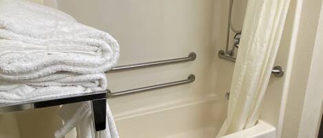A bathroom with a bathtub, a shower, and a towel rack with folded towels.