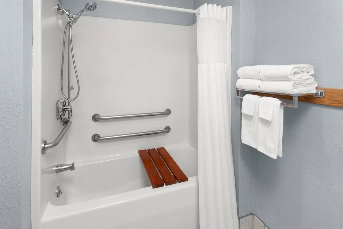 A bathroom with a bathtub, shower, and a towel rack with folded towels.