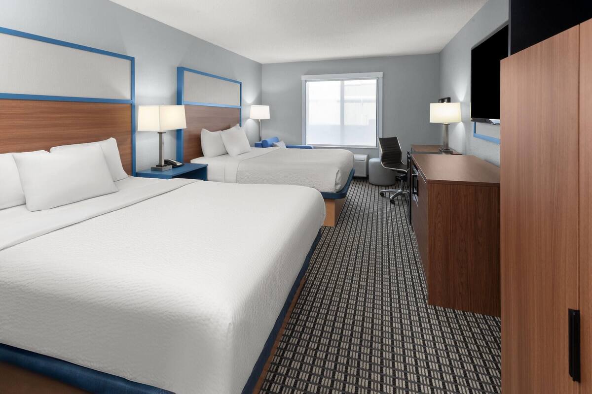 A hotel room with two beds, a desk, a chair, a TV, and a window.