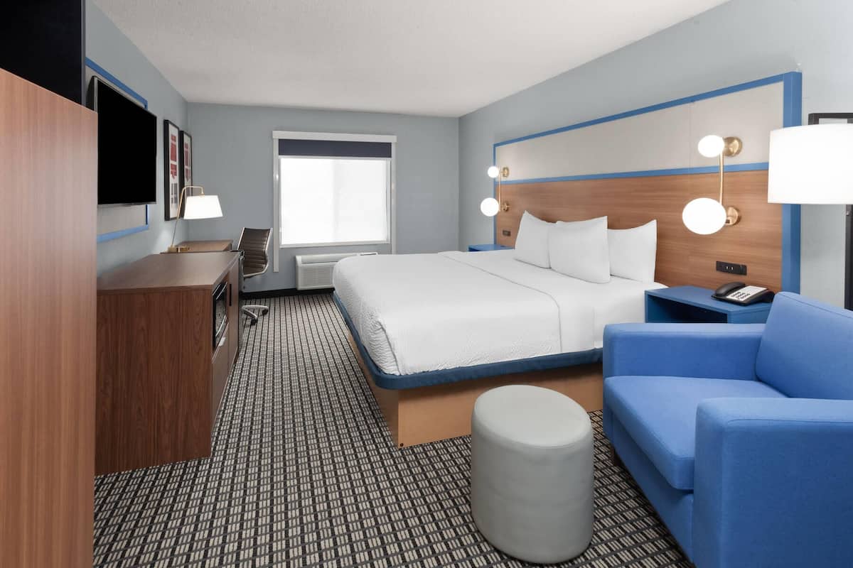 A hotel room with a bed, a desk, a chair, a sofa, a lamp, and a bedside table.