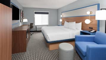 Una habitación de hotel con cama, escritorio, silla, sofá, lámpara y mesita de noche.