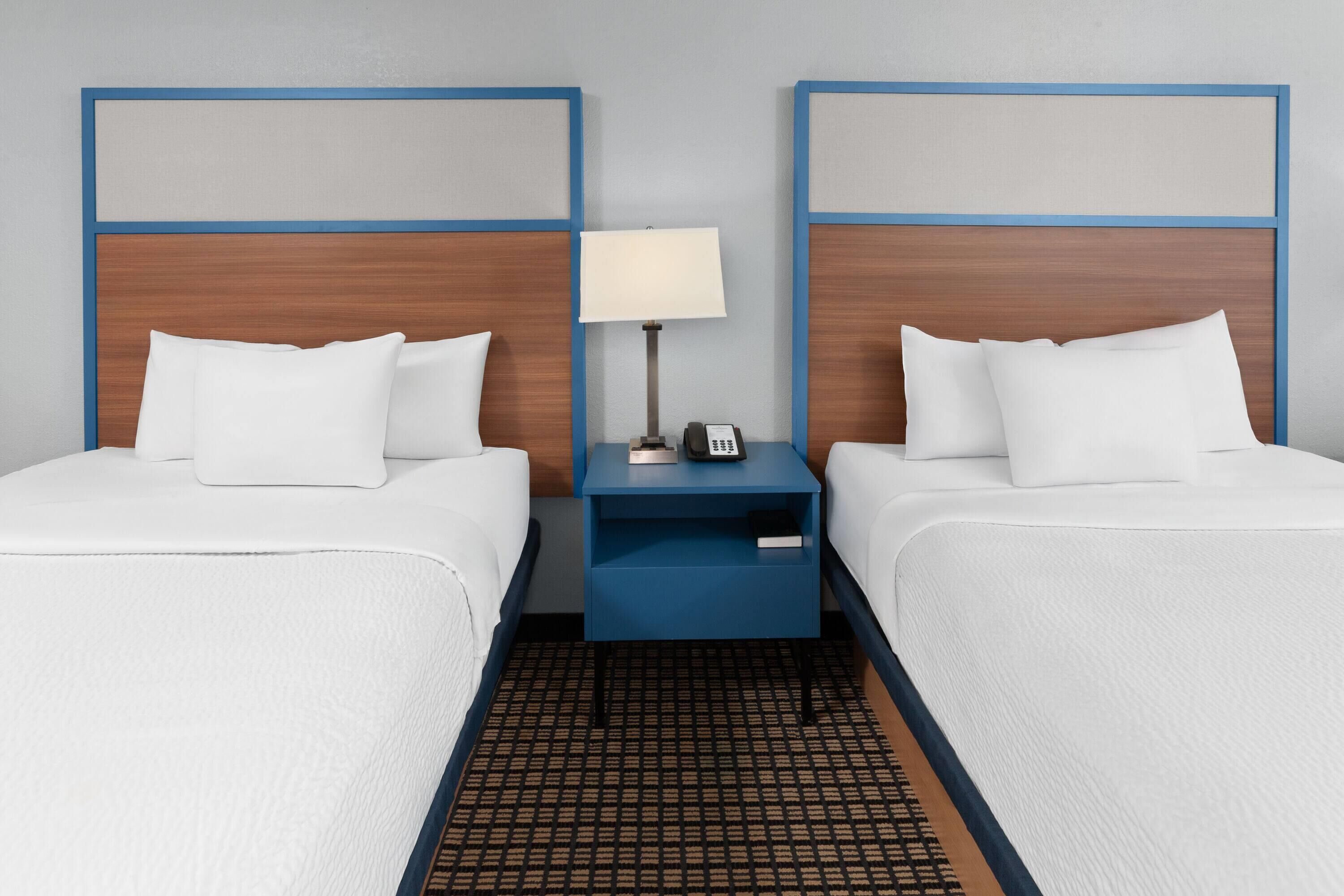 A hotel room with two beds, a nightstand with a lamp, and a phone.