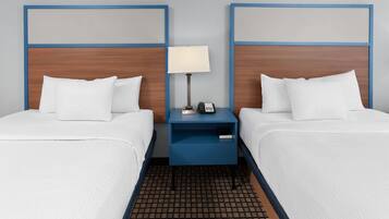 A hotel room with two beds, a nightstand with a lamp, and a phone.
