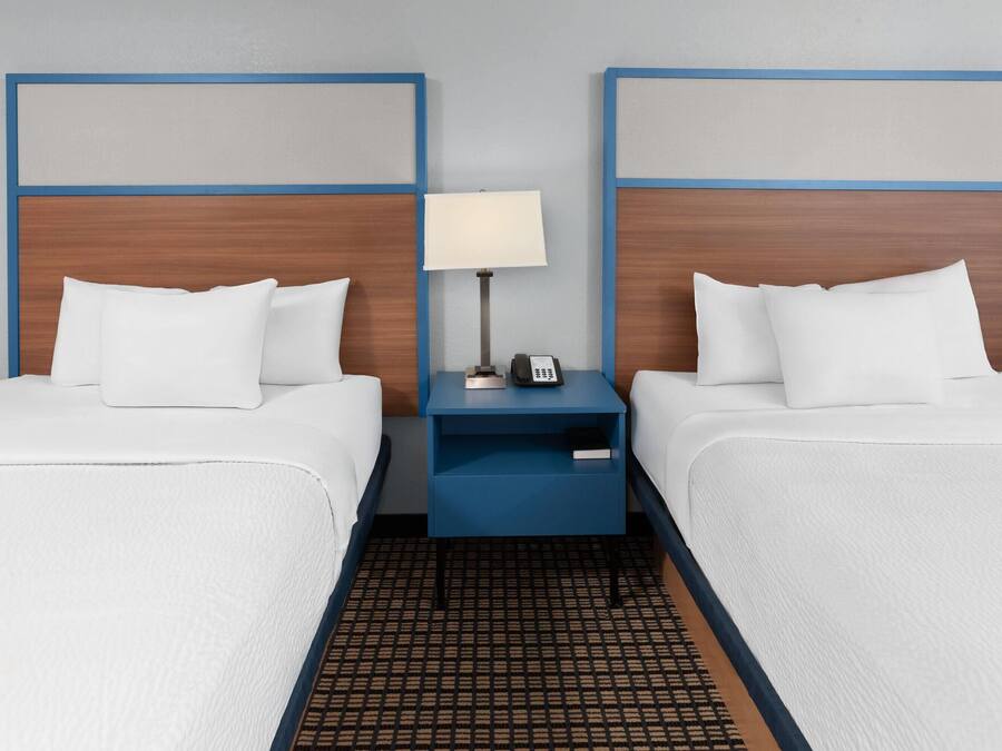 A hotel room with two beds, a nightstand with a lamp, and a phone.