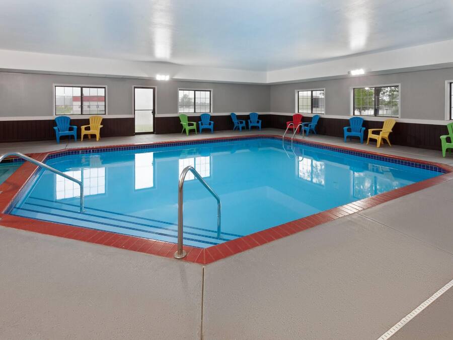 Une piscine intérieure bordée de carreaux, entourée de chaises Adirondack aux couleurs vives, et dotée de grandes fenêtres le long des murs.