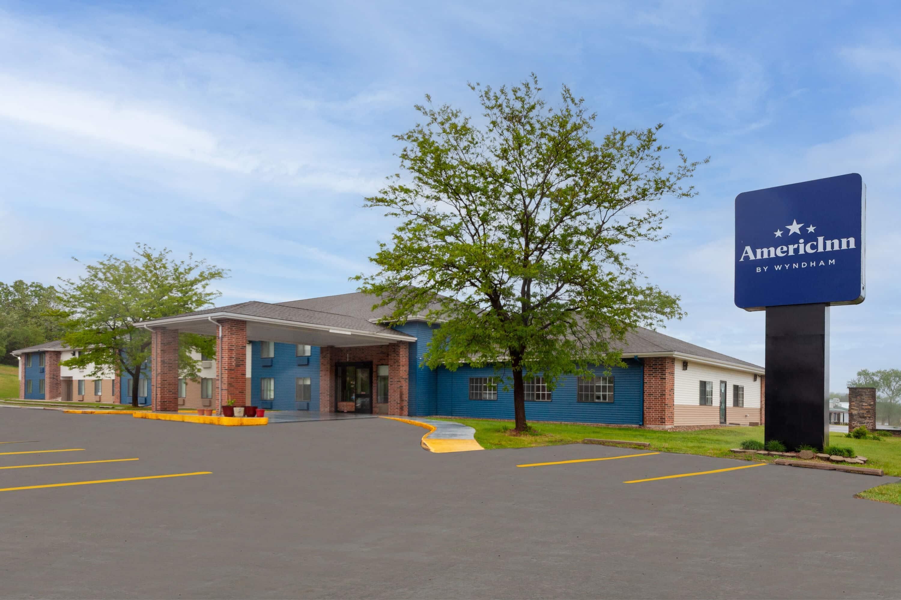 Un motel con fachada azul, zona de estacionamiento techada y un cartel que indica que pertenece a Wyndham.