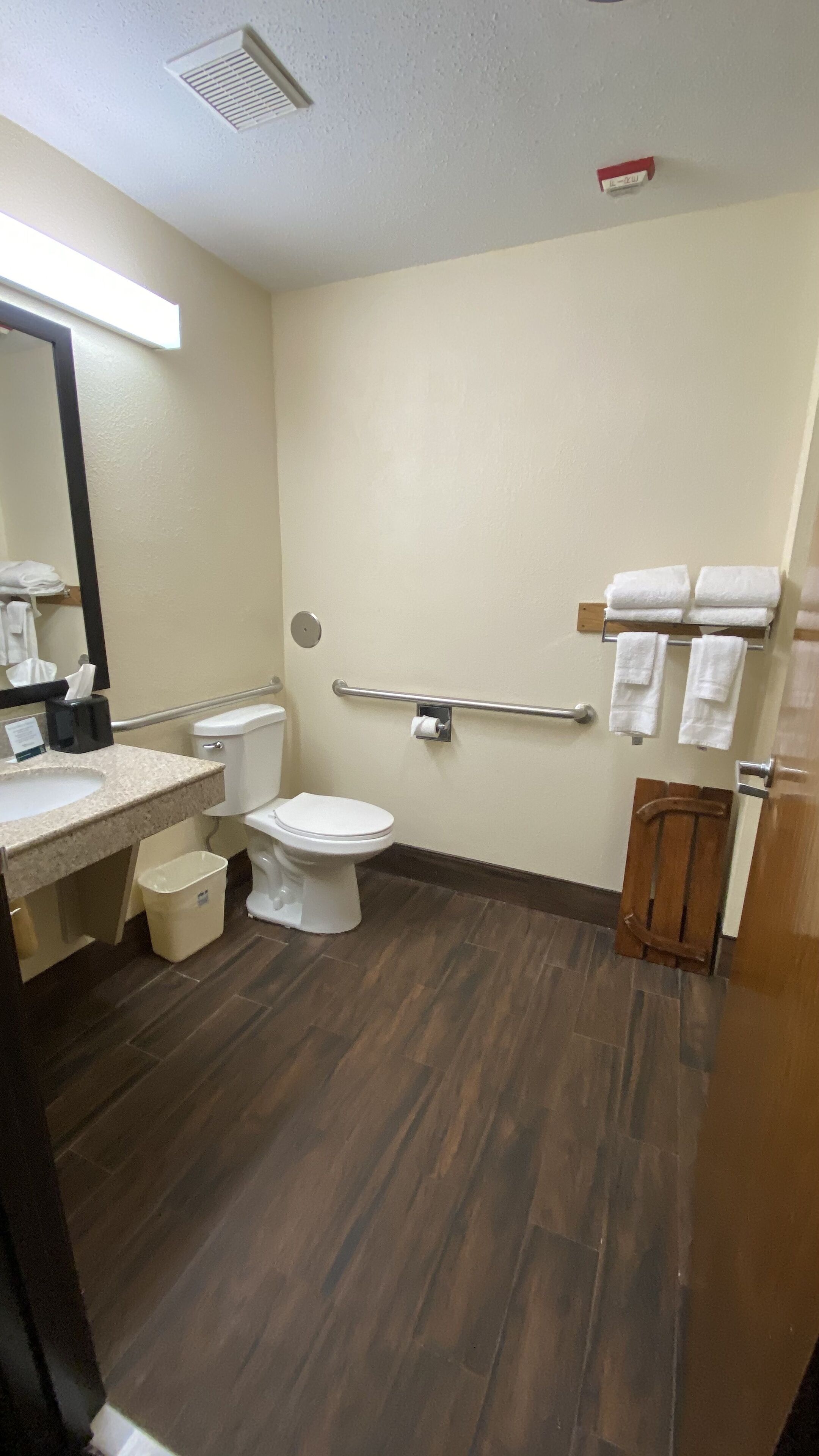 Un baño con inodoro, lavamanos y barras de apoyo.