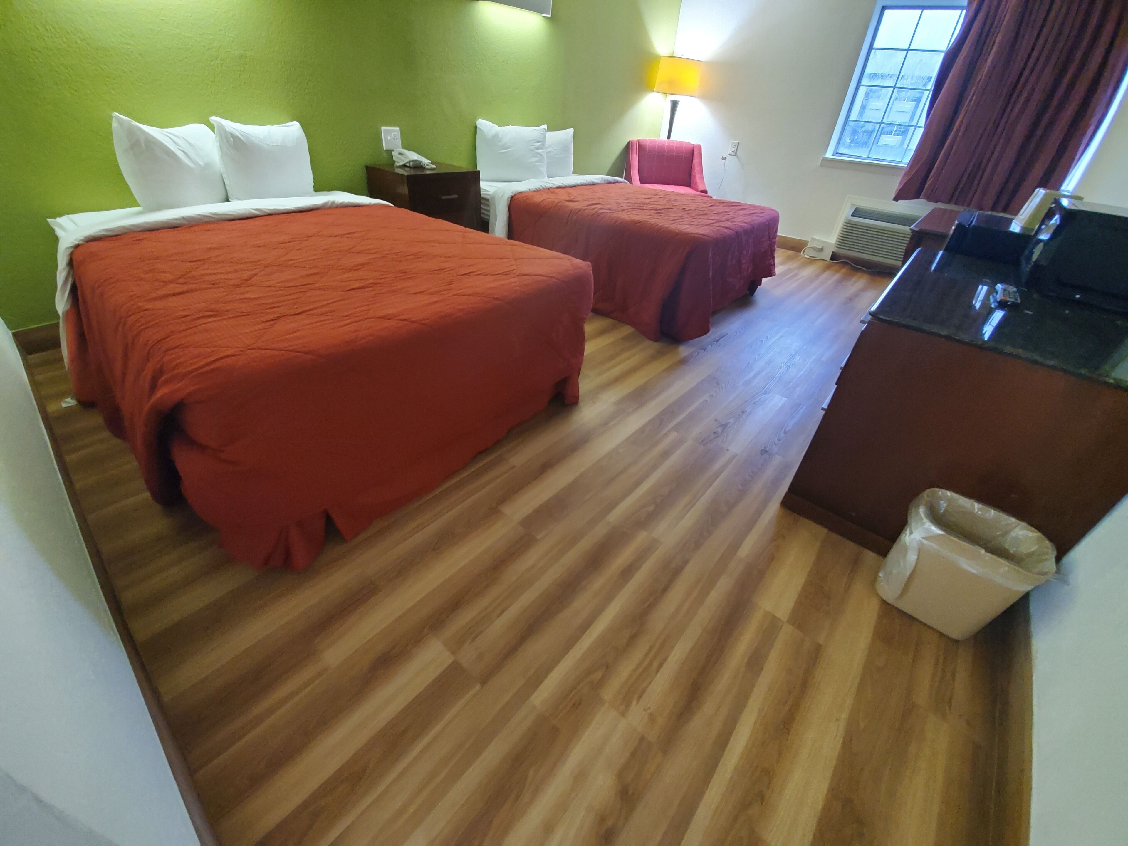 A hotel room with two beds, a desk, a trash bin, and a window with curtains.