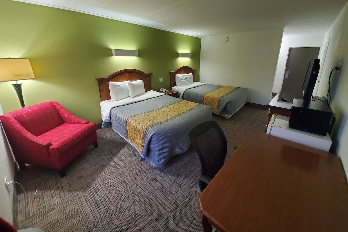 A hotel room with two beds, a red armchair, a wooden desk, and a television.