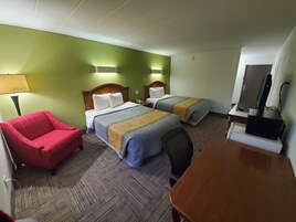 Habitación de hotel con dos camas, un sillón rojo, un escritorio de madera y un televisor.