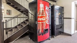 Una máquina expendedora de Coca-Cola junto a una escalera y un refrigerador.
