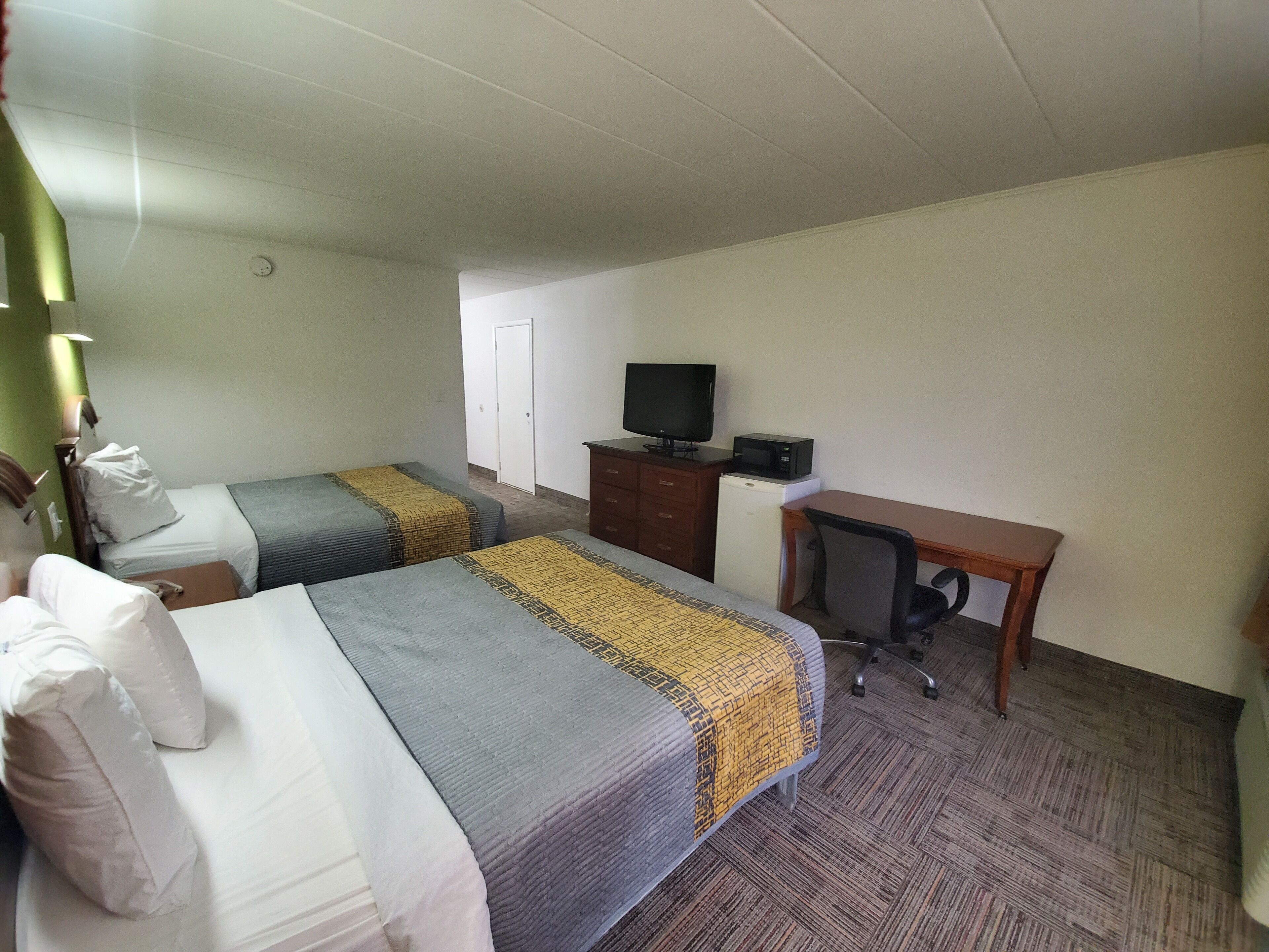 A hotel room with two beds, a desk, a television, and a microwave.