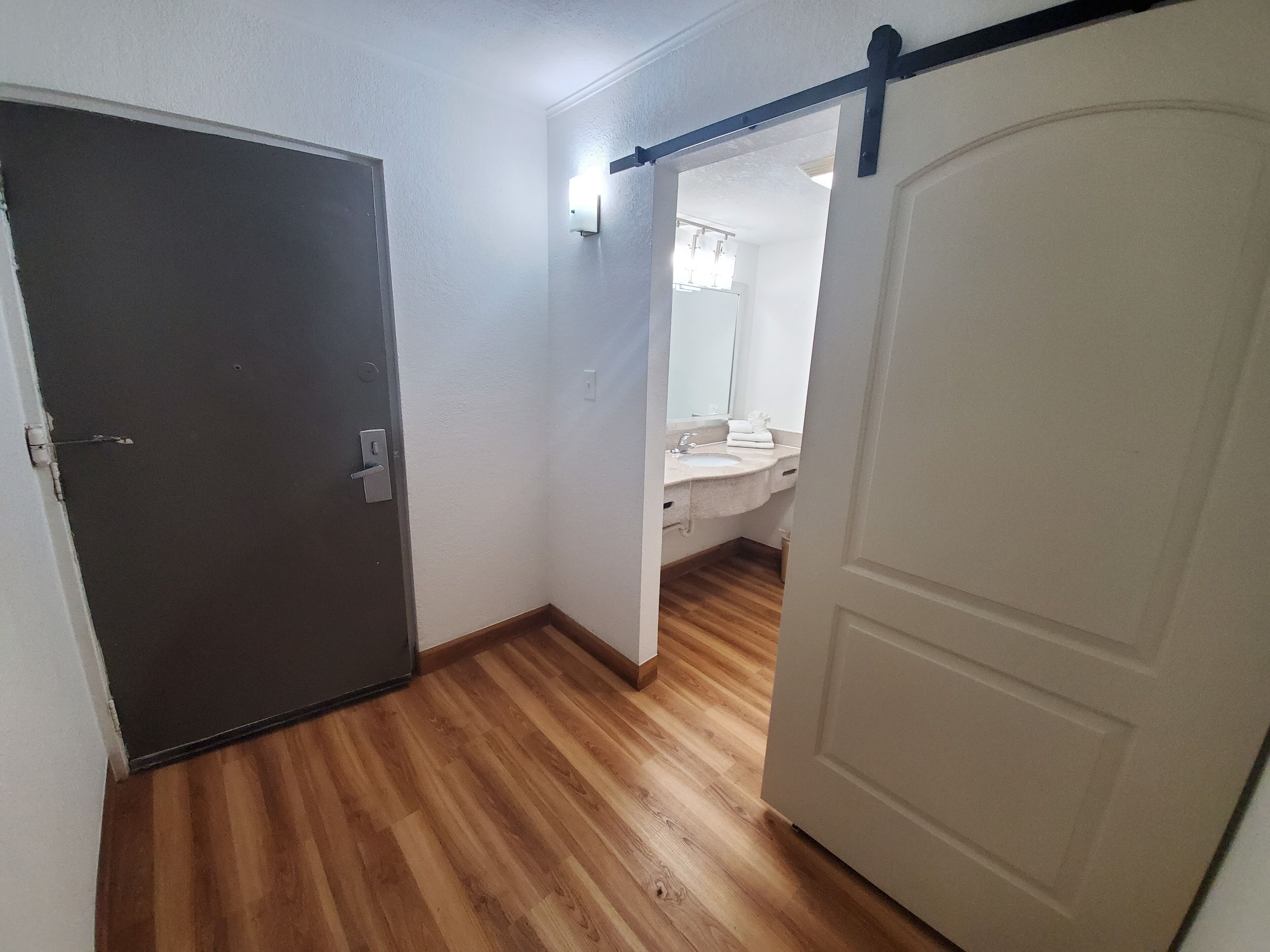 A hallway with wooden flooring leading to a bathroom with a sink and mirror.