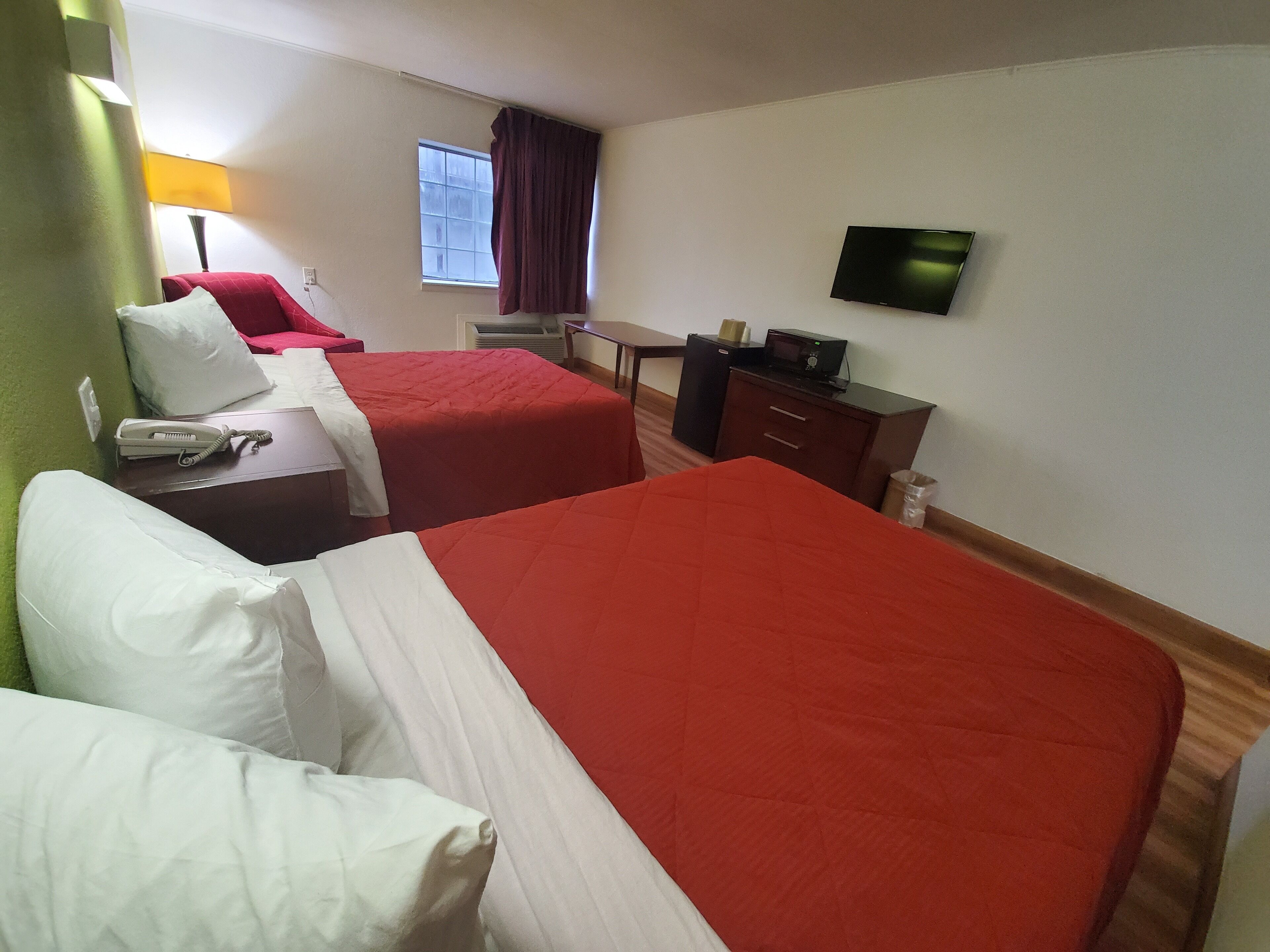 A hotel room with two beds, a desk, a television, and a window with curtains.