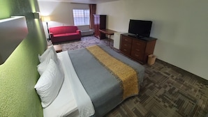 Una habitación de hotel con cama, un sofá rojo, un televisor sobre un mueble de madera y una ventana con cortinas.