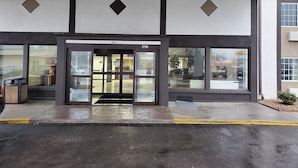 Un edificio con una amplia entrada de vidrio, un número de dirección visible y una vista despejada del interior a través de las puertas de cristal.