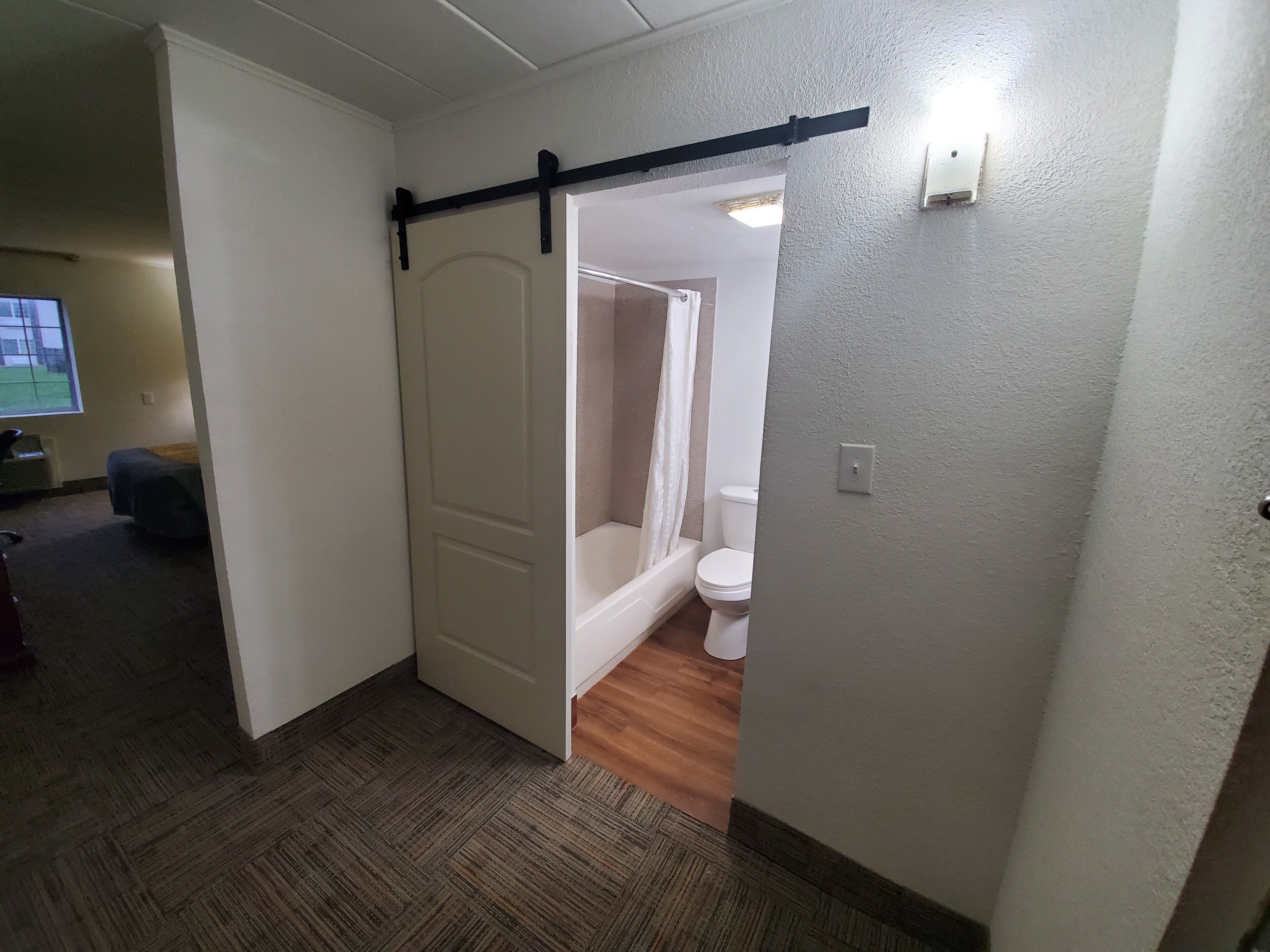 Habitación de hotel con suelo de madera y una puerta corredera que da a un baño con inodoro y ducha.