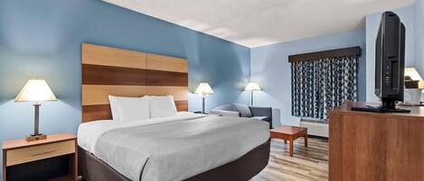 Une chambre d’hôtel avec un grand lit, deux tables de chevet avec des lampes, un bureau avec une télévision et un rideau à motifs.