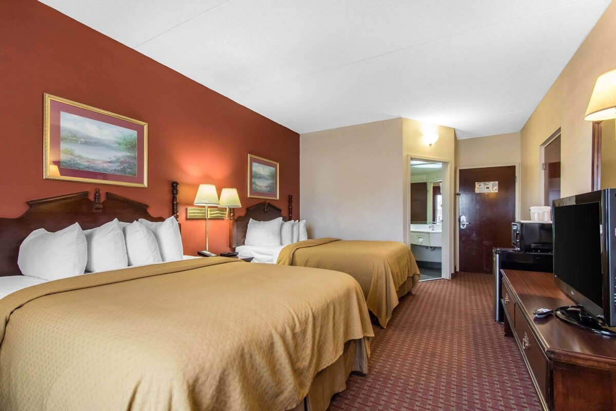 A hotel room with two beds, a TV, a desk, and a bathroom visible through an open door.