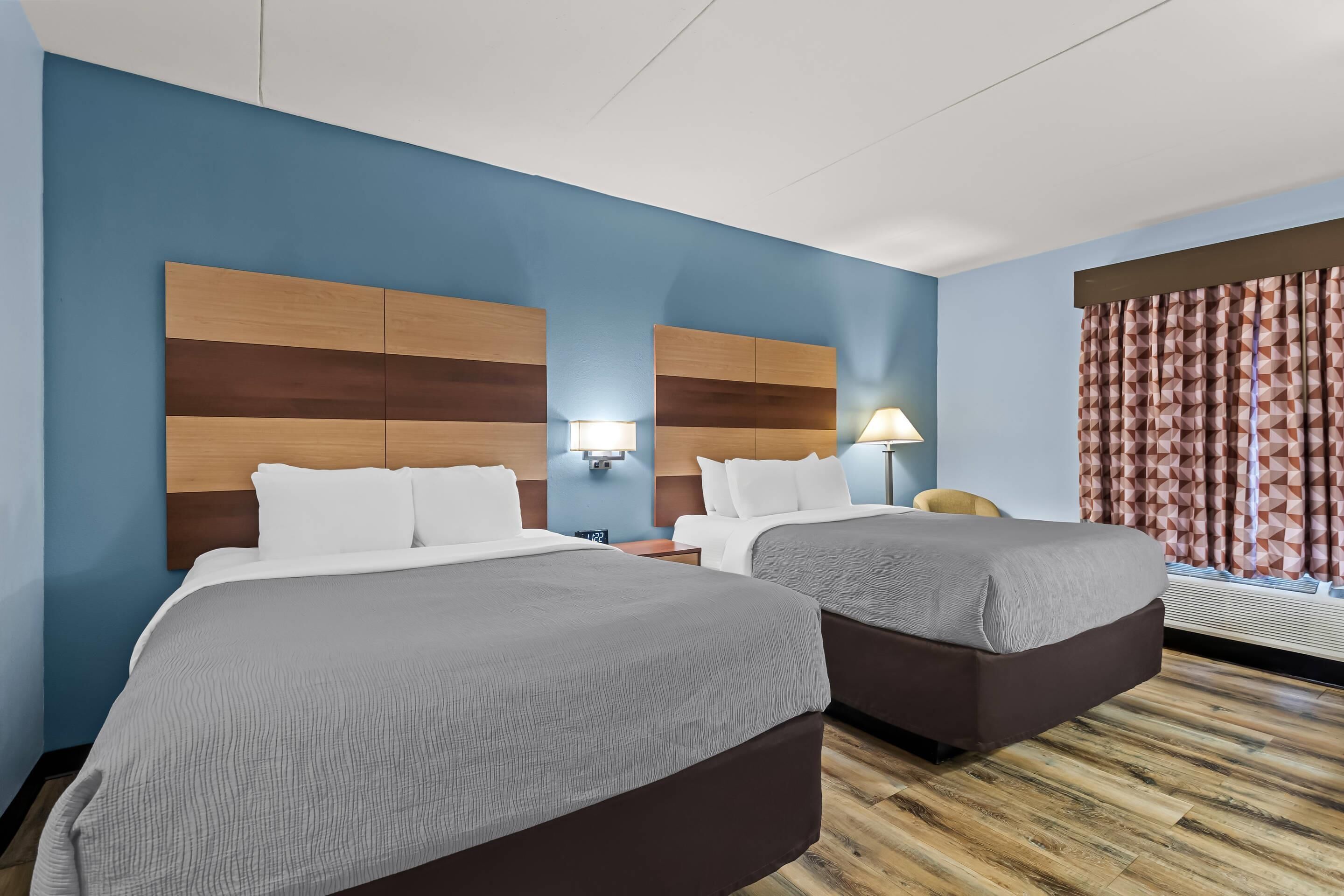 A hotel room with two beds, a nightstand, a lamp, and a window with patterned curtains.