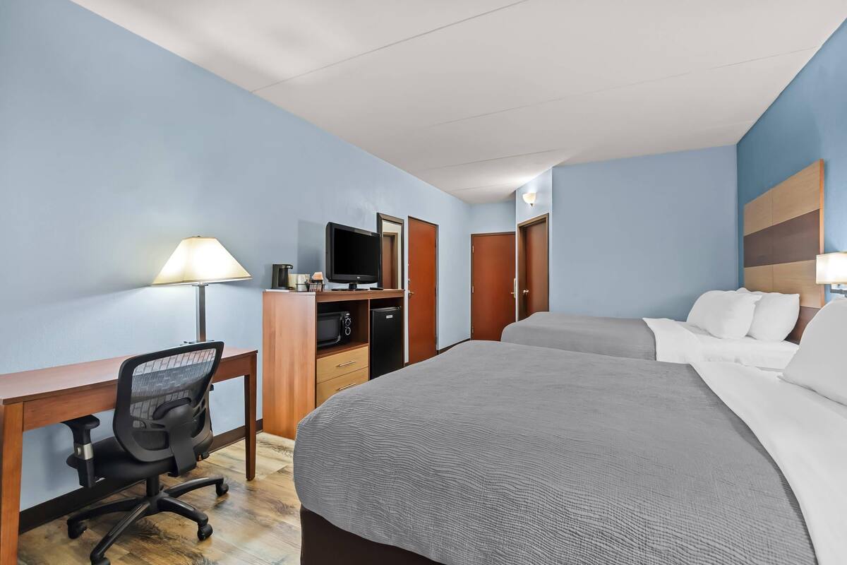 A hotel room with a large bed, a desk with a chair, a television, and a wardrobe.