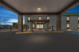 Una entrada de edificio con un vestíbulo techado, pilares de piedra y una puerta de cristal.