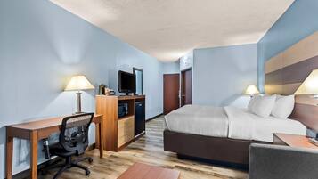 A hotel room with a bed, desk, chair, TV, and a small kitchenette.