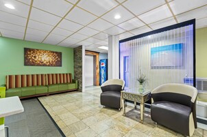 Un hall con una pared verde, una zona de estar con un sofá, dos sillones, una mesita y una pared decorativa con el logotipo de Pepsi.