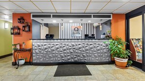 A hotel reception area with a modern design, featuring a geometric-patterned counter, a reception desk, and a large potted plant. - Quality Inn Hixson - Chattanooga (Hixson)
