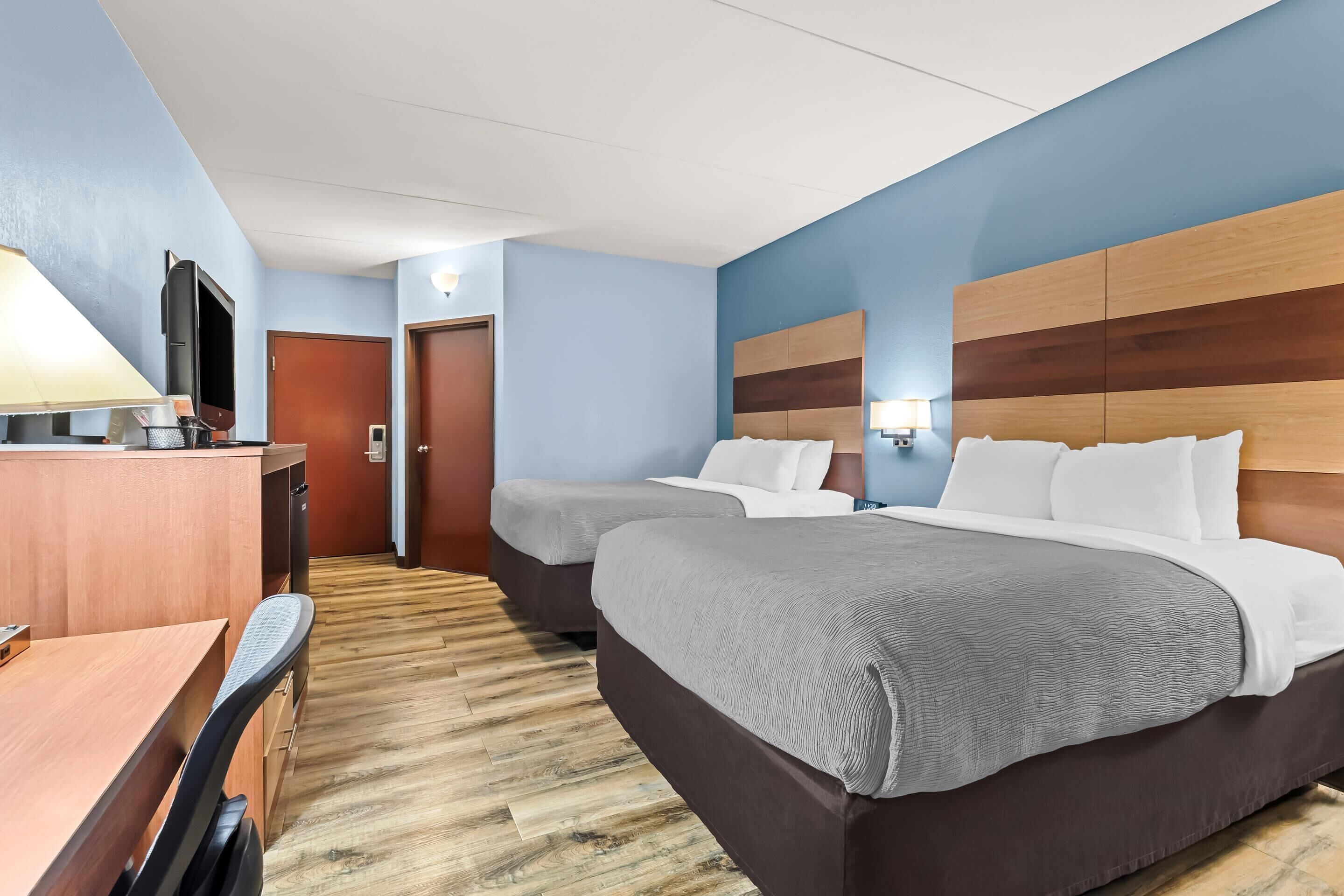 A hotel room with two beds, a desk, a chair, and a television.
