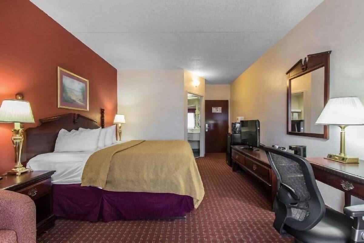 A hotel room with a bed, desk, television, and a mirror.