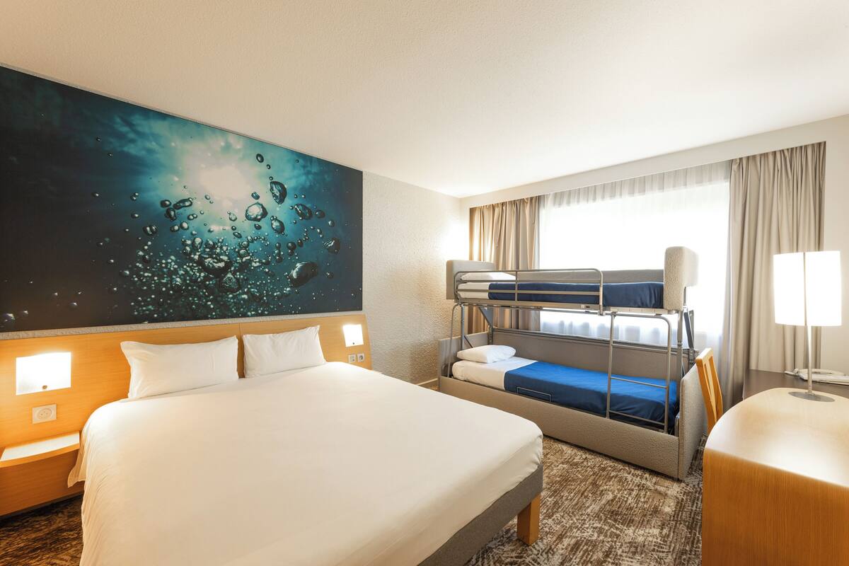Ein Hotelzimmer mit einem großen Bett, einem Etagenbett, einem Schreibtisch und einem Wandbild.
