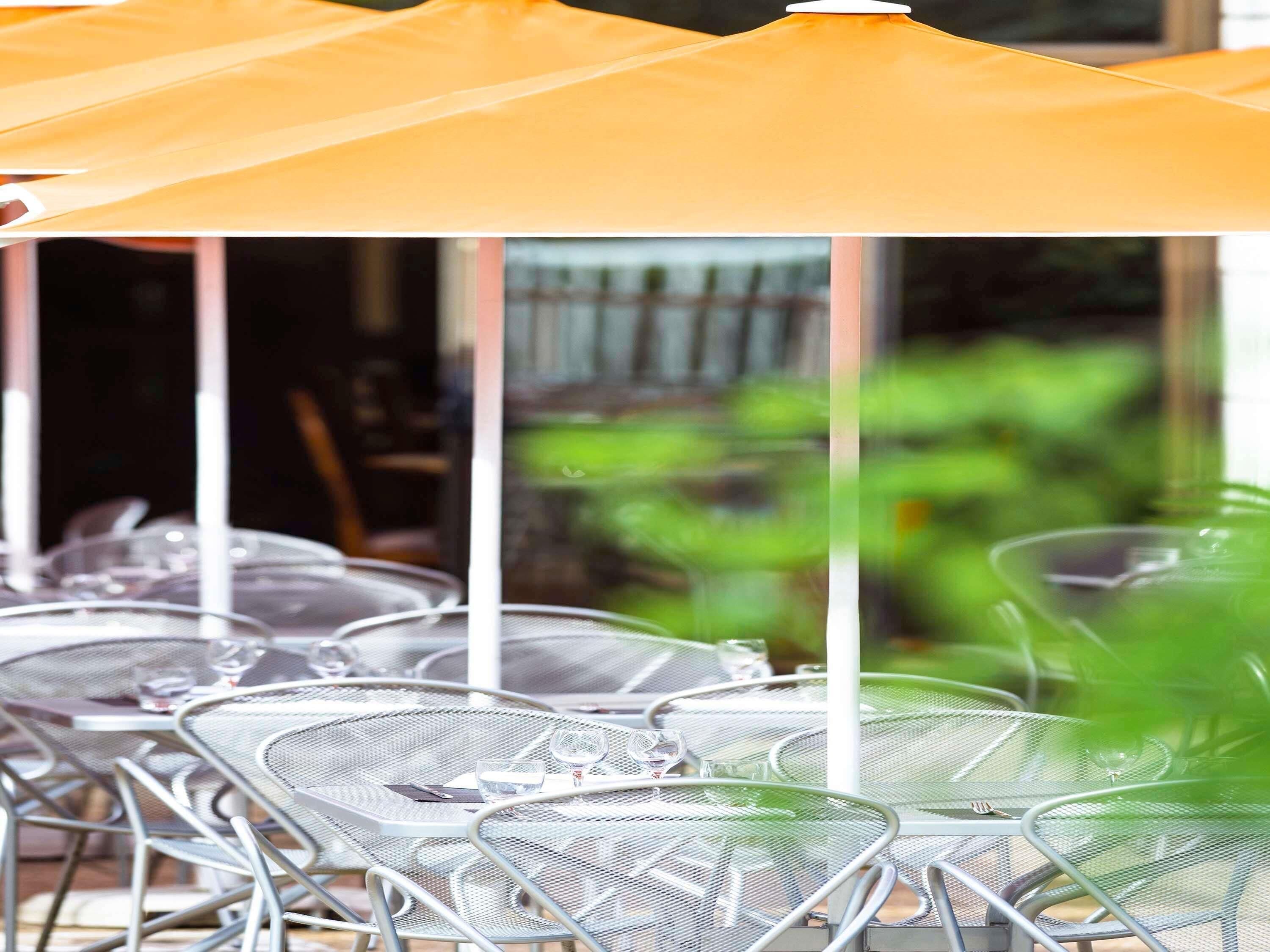 Outdoor seating with metal chairs and tables, covered by a large umbrella.