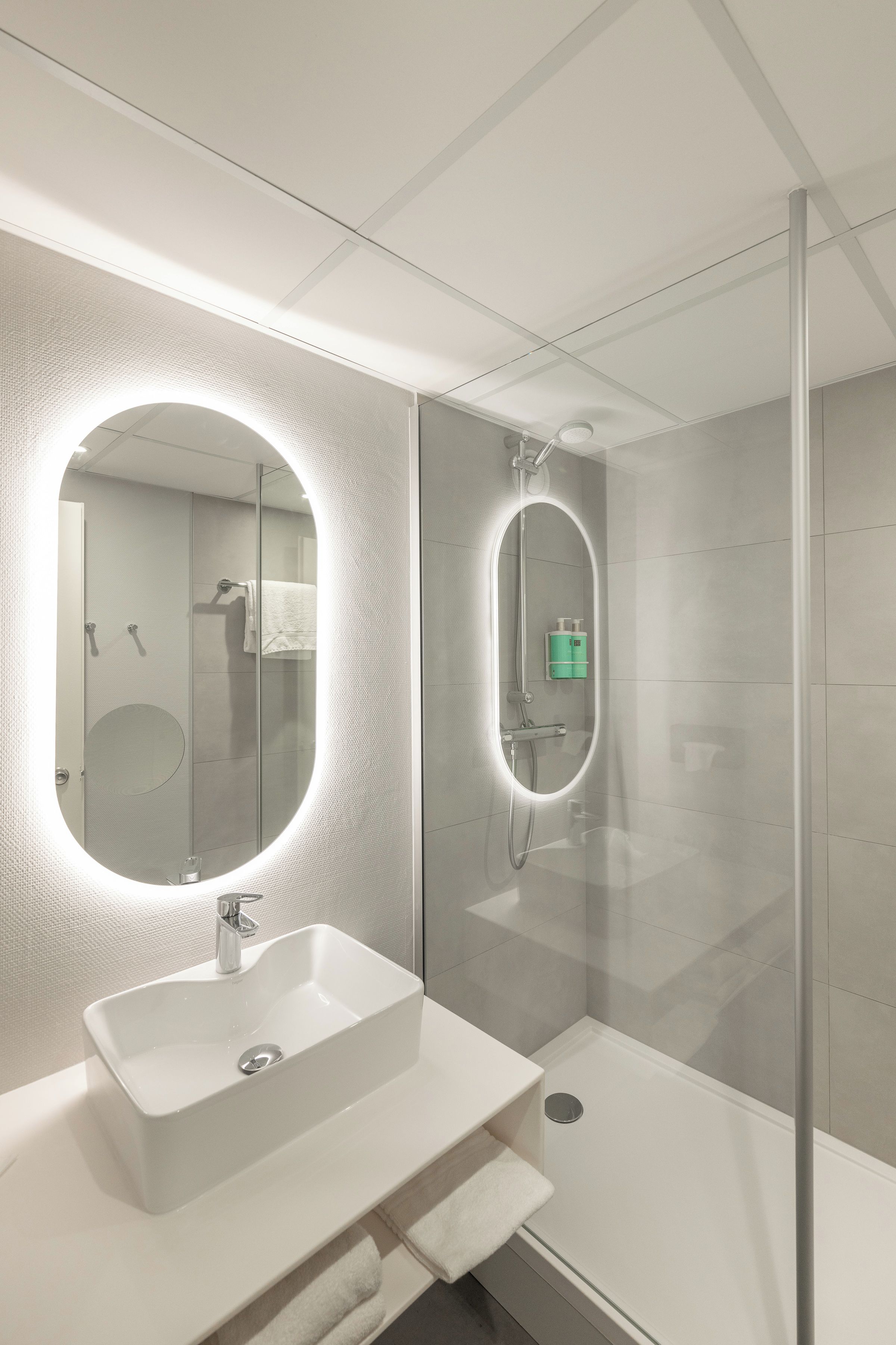 Un bagno moderno con cabina doccia in vetro, lavandino bianco e un ampio specchio ovale.