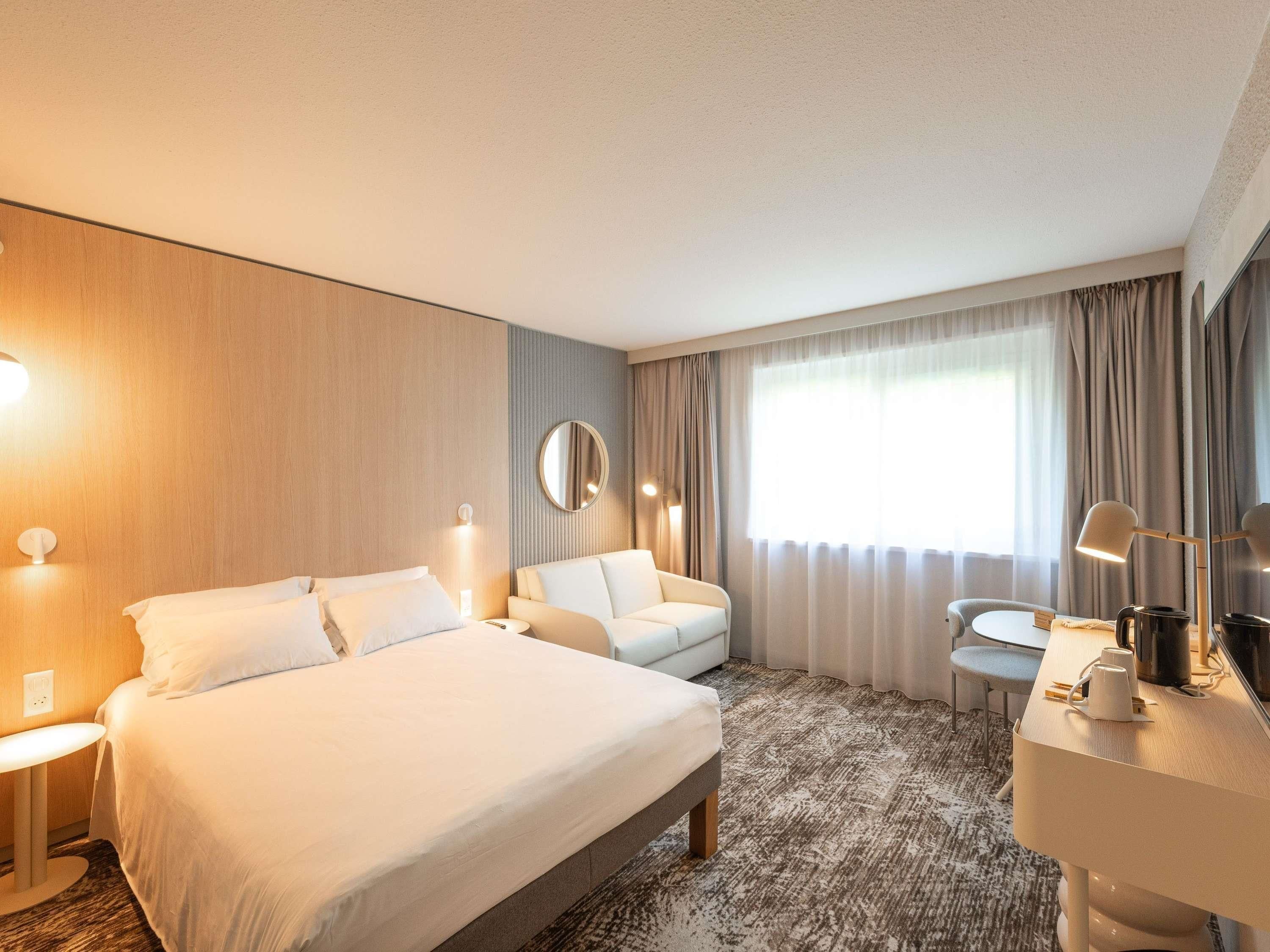A hotel room with a bed, a sofa, a desk, and a mirror.