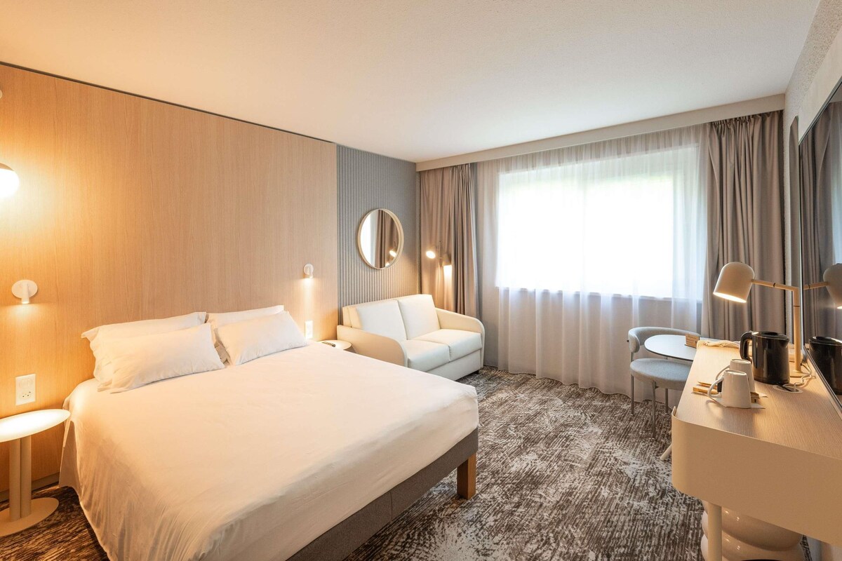 Una habitación de hotel con cama, sofá, escritorio y espejo.