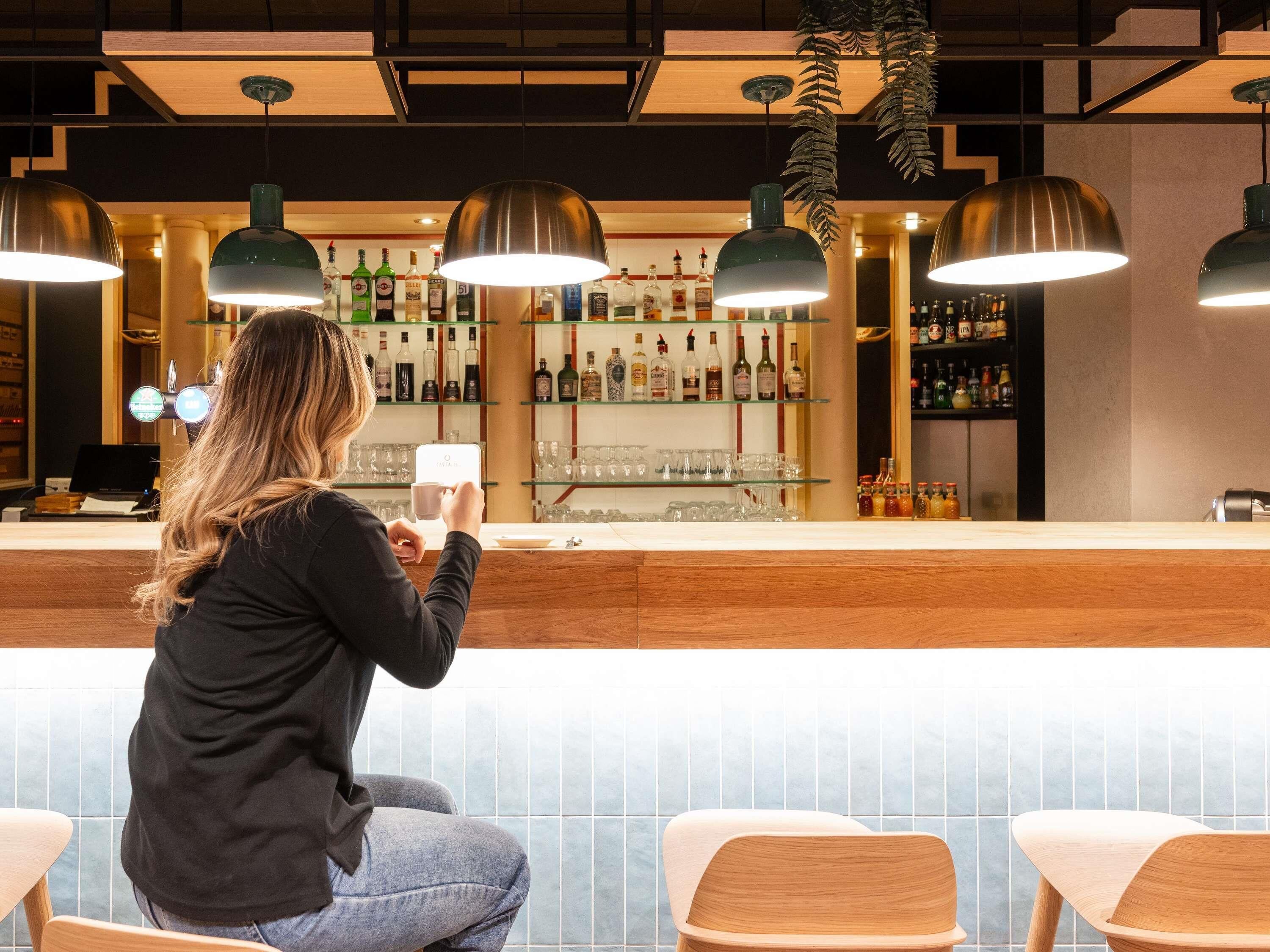 Una persona sentada en un bar, con una barra que muestra diferentes botellas y vasos.