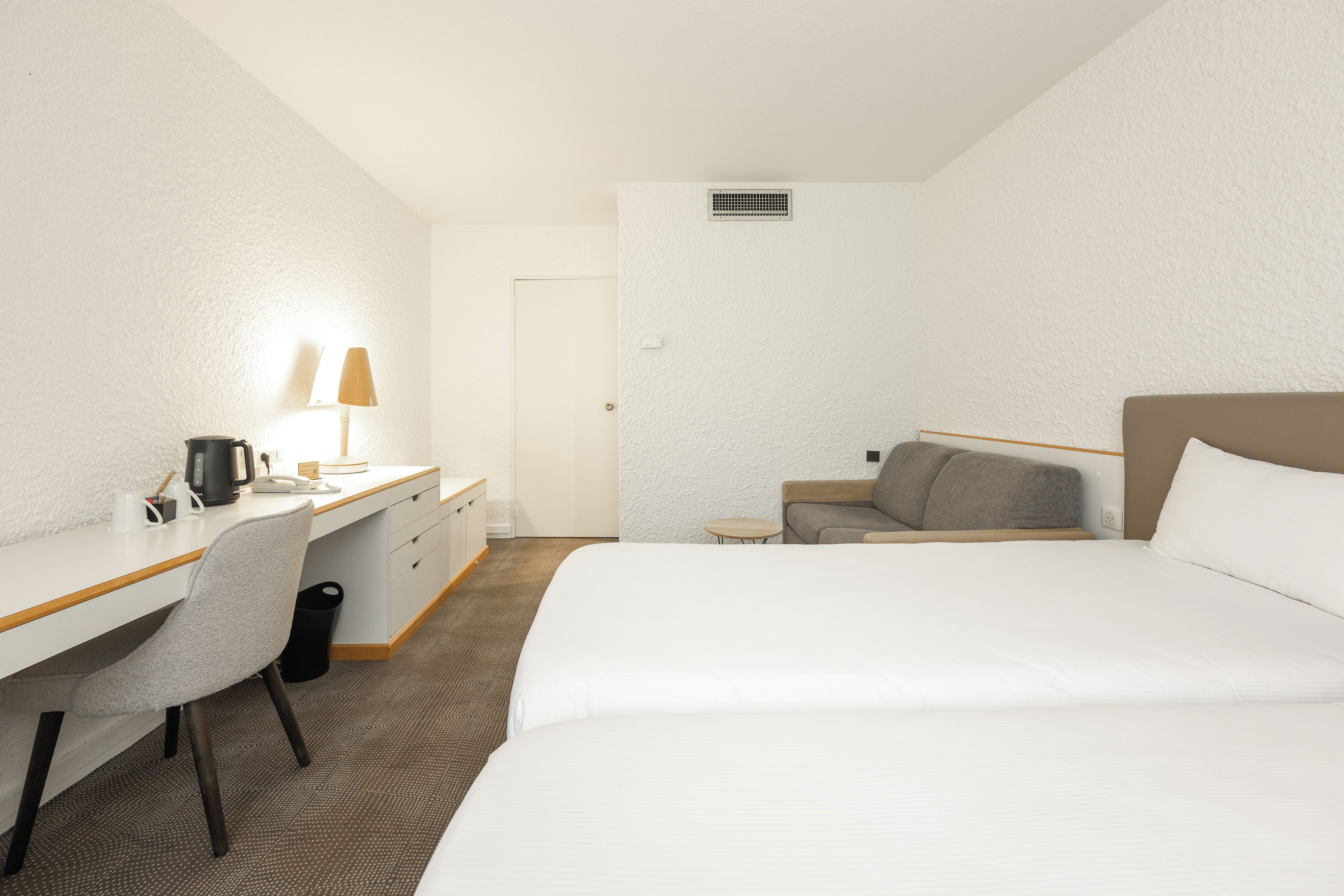 A hotel room with a bed, a desk with a lamp, a chair, a small table, and a sofa.