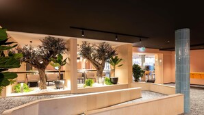 A modern hotel lobby with seating areas, potted plants, and a reception desk. - Novotel Mâcon Nord – Porte de Bourgogne (Macon)