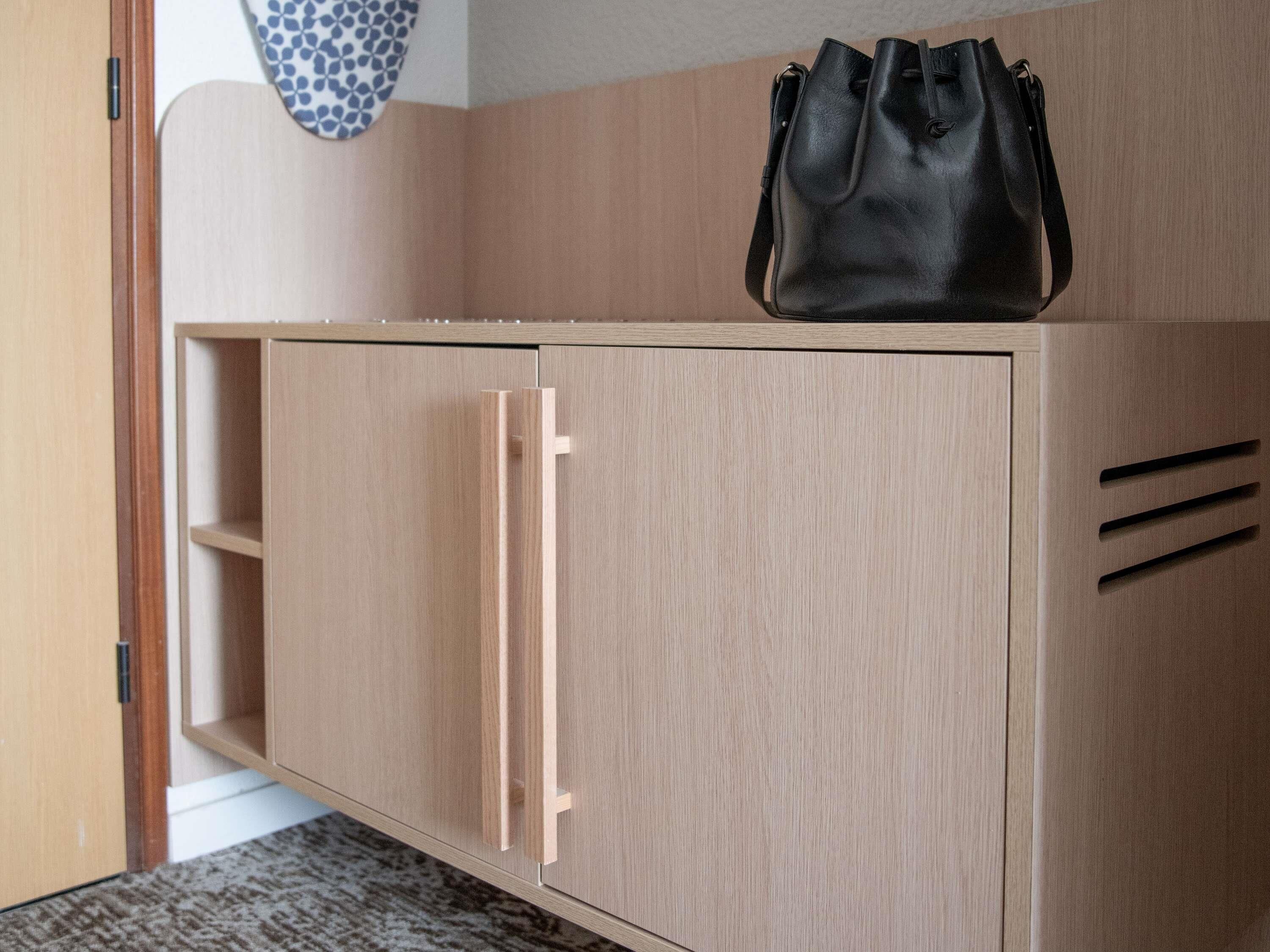 A wooden wardrobe with a hanging bag, a door, and a shelf.
