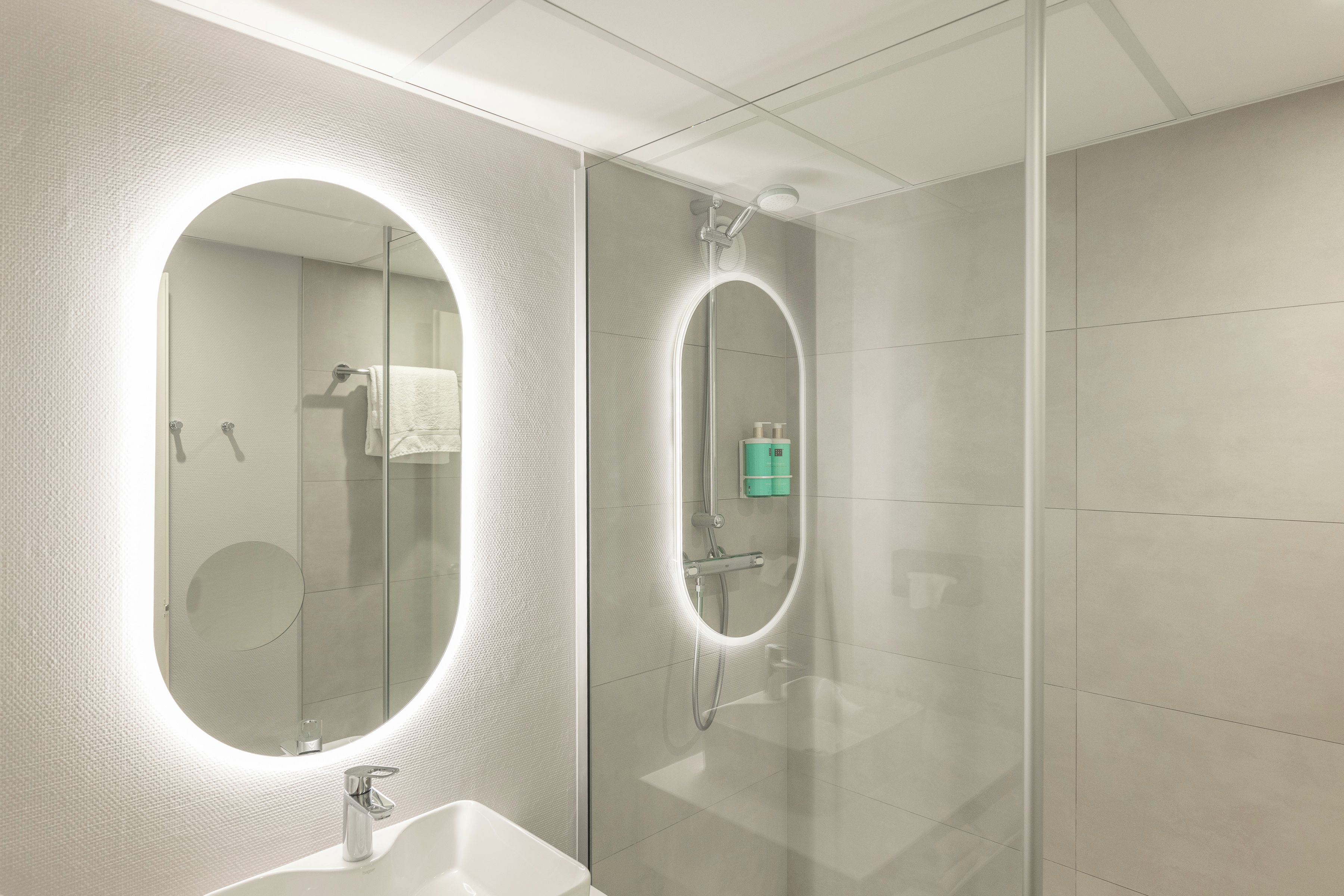 A modern bathroom with a large mirror, a sink, and a shower area.